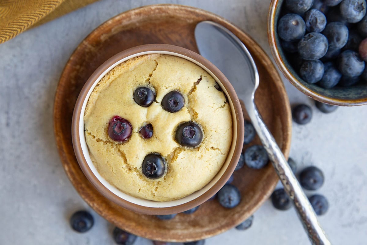 Blueberry muffin in a ramekin with fresh berries to the side.