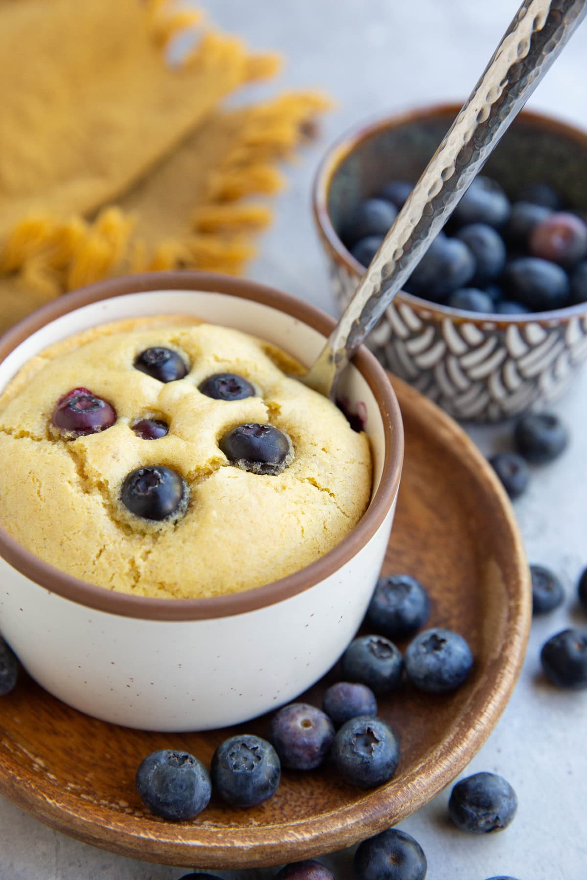 Blueberry muffin in a ramekin with a spoon. Fresh berries all around. Ready to eat.
