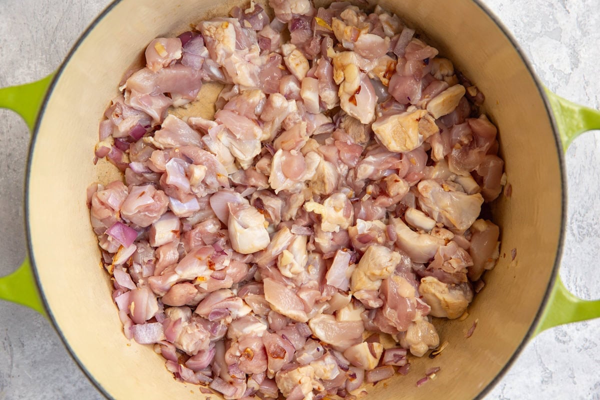 Chopped chicken thighs cooking in a large pot.