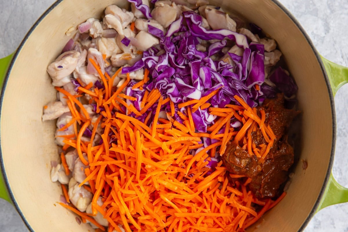 Large pot full of chicken, grated carrots, cabbage, and Thai sauce.