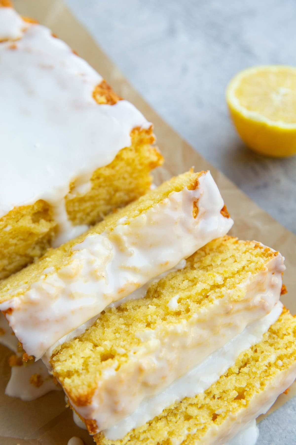 Loaf of iced lemon pound cake cut into slices with a lemon in the background.