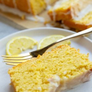 Slice of lemon pound cake on a white plate the fresh lemon slices and a golden fork.