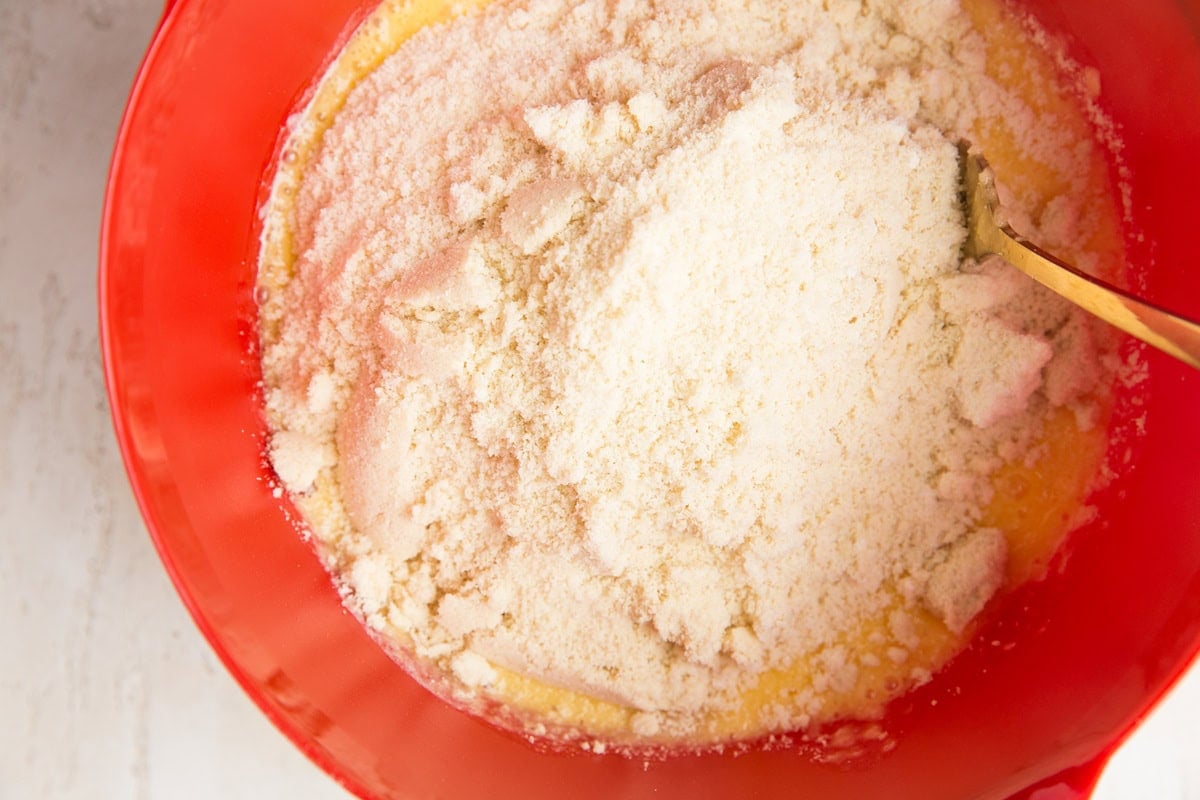 Dry ingredients on top of wet ingredients in a red mixing bowl to make lemon pound cake.