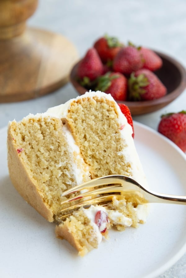 Fork taking a bite of vanilla layer cake.