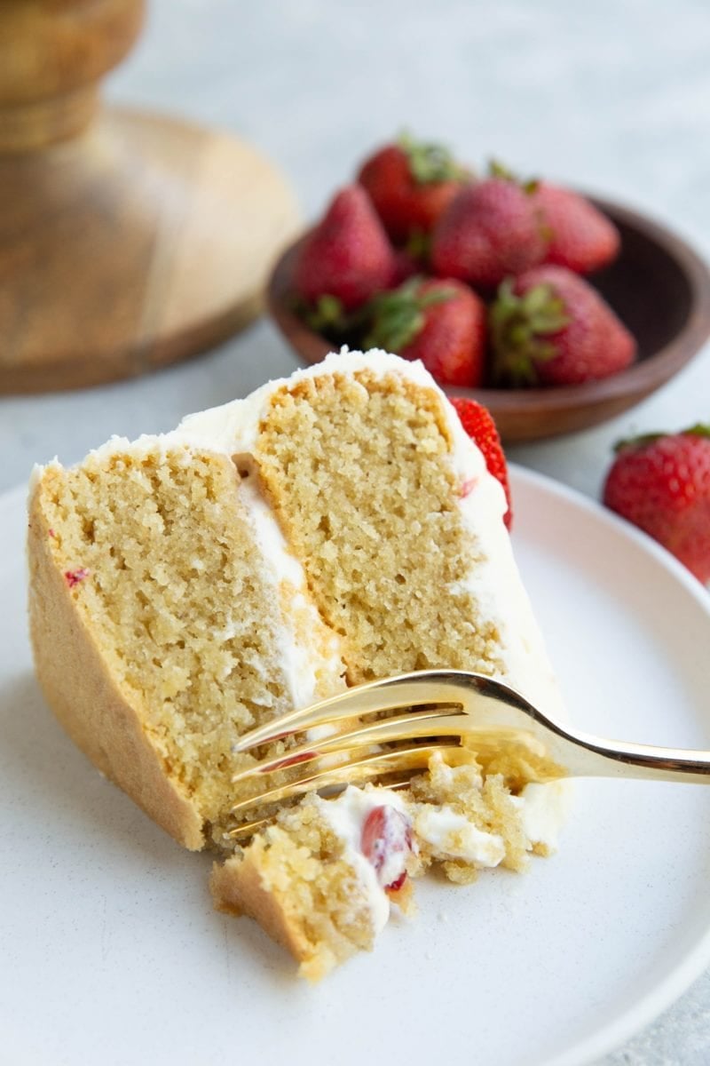 Fork taking a bite of vanilla layer cake.