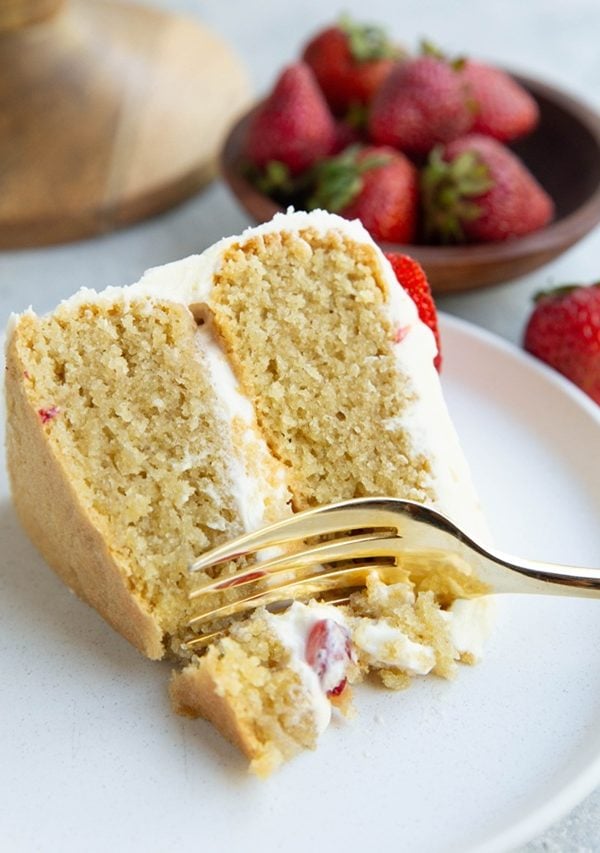 Slice of almond flour vanilla cake on a white plate with a fork taking a bite out of the cake.