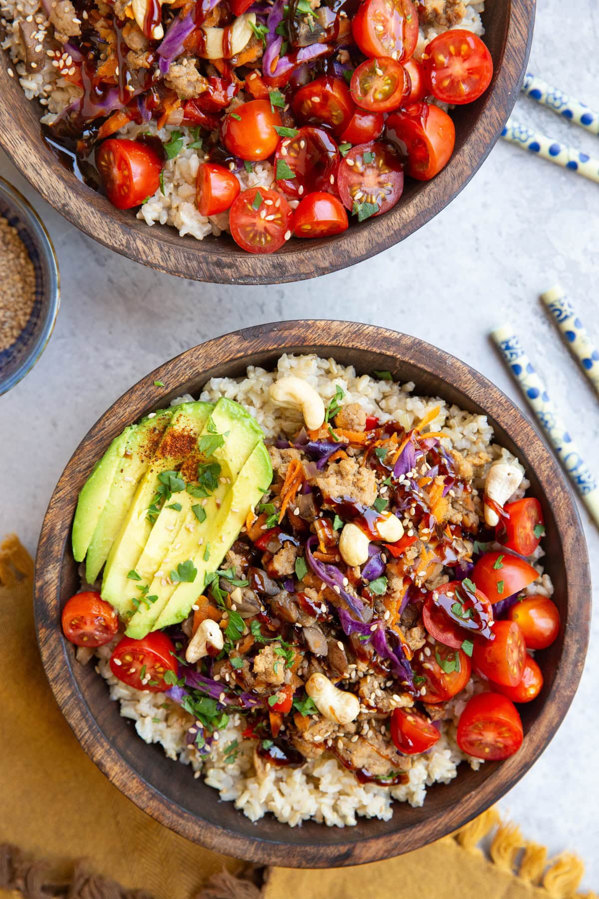Two large wooden bowls filled with brown rice, Asian ground turkey with vegetables, avocado, tomatoes and chopsticks to the side and a golden napkin. Ready to eat.
