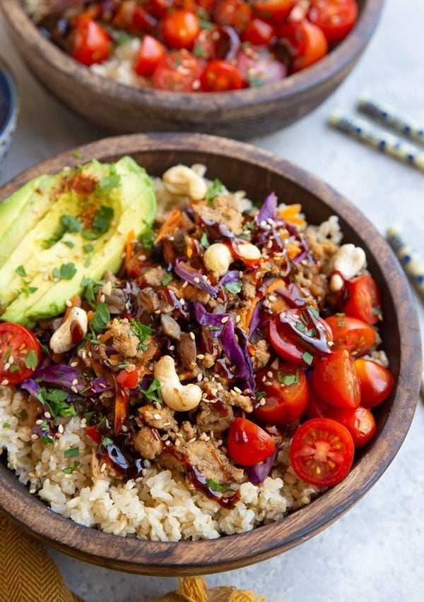 Wooden bowl full of ground turkey with fresh vegetables and a sauce drizzled on top.