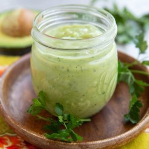 Jar full of avocado dressing with fresh parsley all around and half of an avocado in the background.