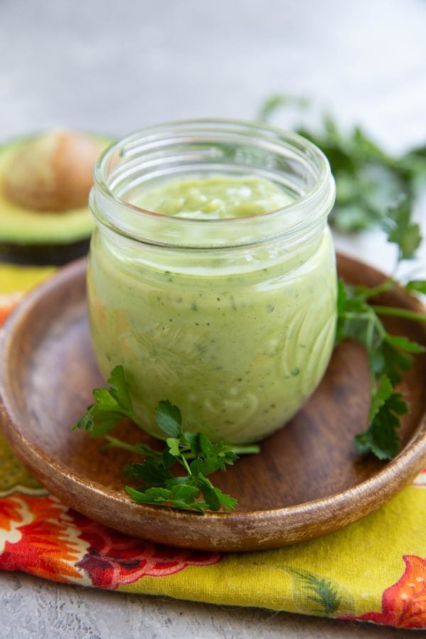 Jar full of avocado dressing with fresh parsley all around and half of an avocado in the background.