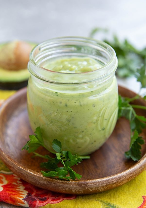 Avocado salad dressing in a small jar with fresh parsley to the side.