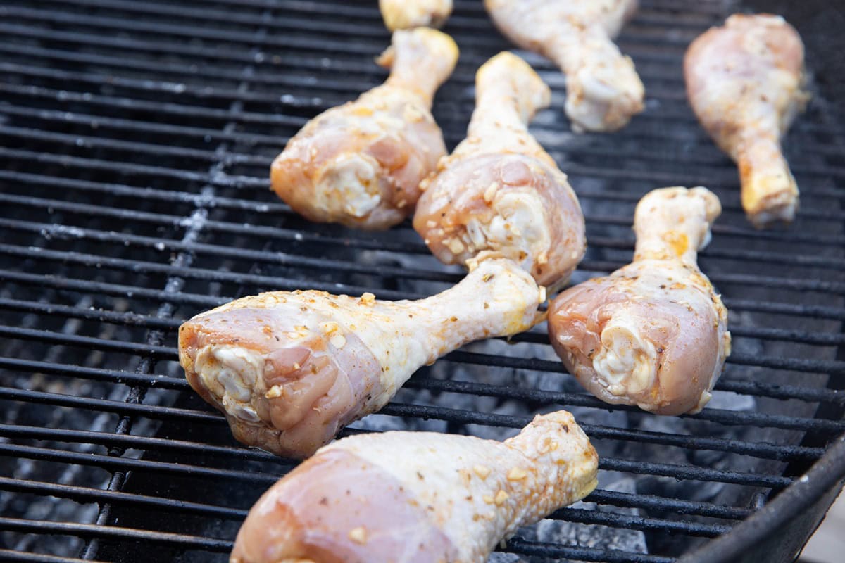 Chicken drumsticks grilling on a charcoal barbecue.