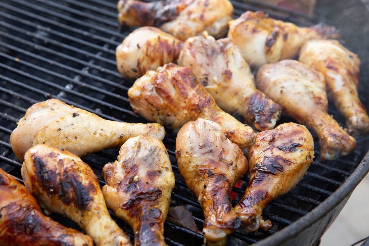 Charcoal barbecue with chicken drumsticks grilling. Golden brown char marks on the chicken legs.