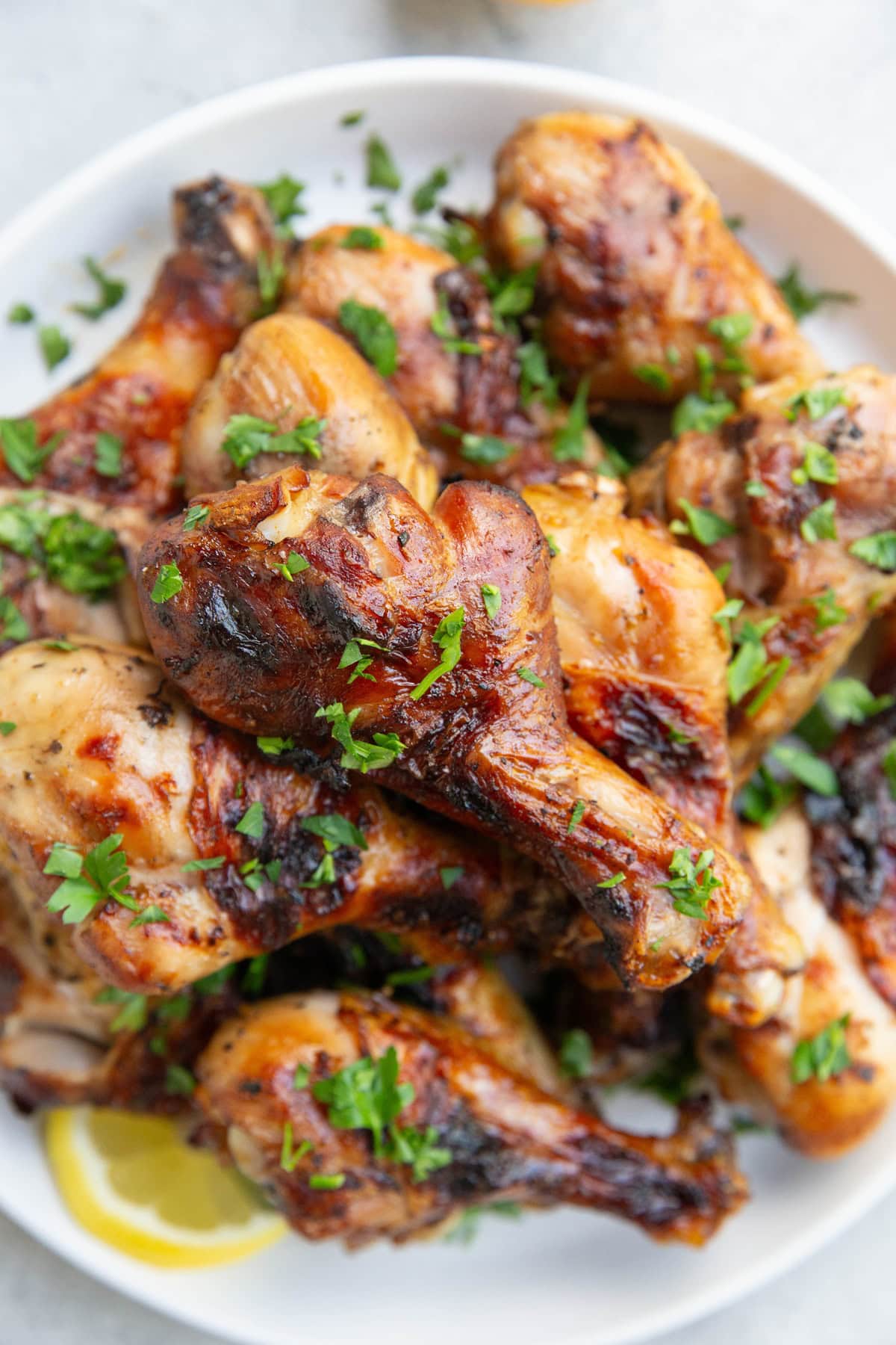 Plate of grilled chicken drumsticks sprinkled with fresh parsley and a slice of lemon to the side. Ready to serve.