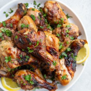 Plate of chicken drumsticks with fresh parsley sprinkled on top and slices of lemons to the side. Ready to serve with side dishes.