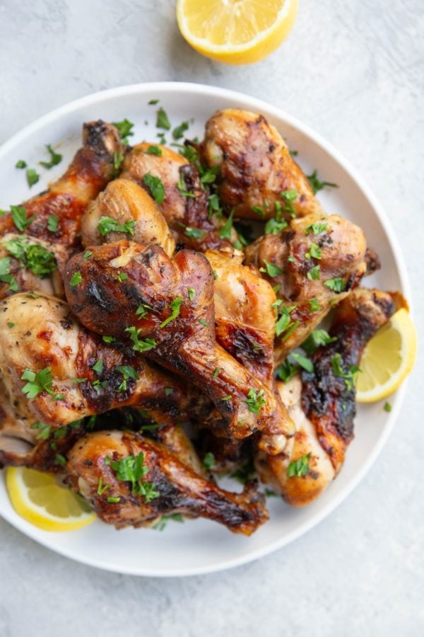 Plate of chicken drumsticks with fresh parsley sprinkled on top and slices of lemons to the side. Ready to serve with side dishes.