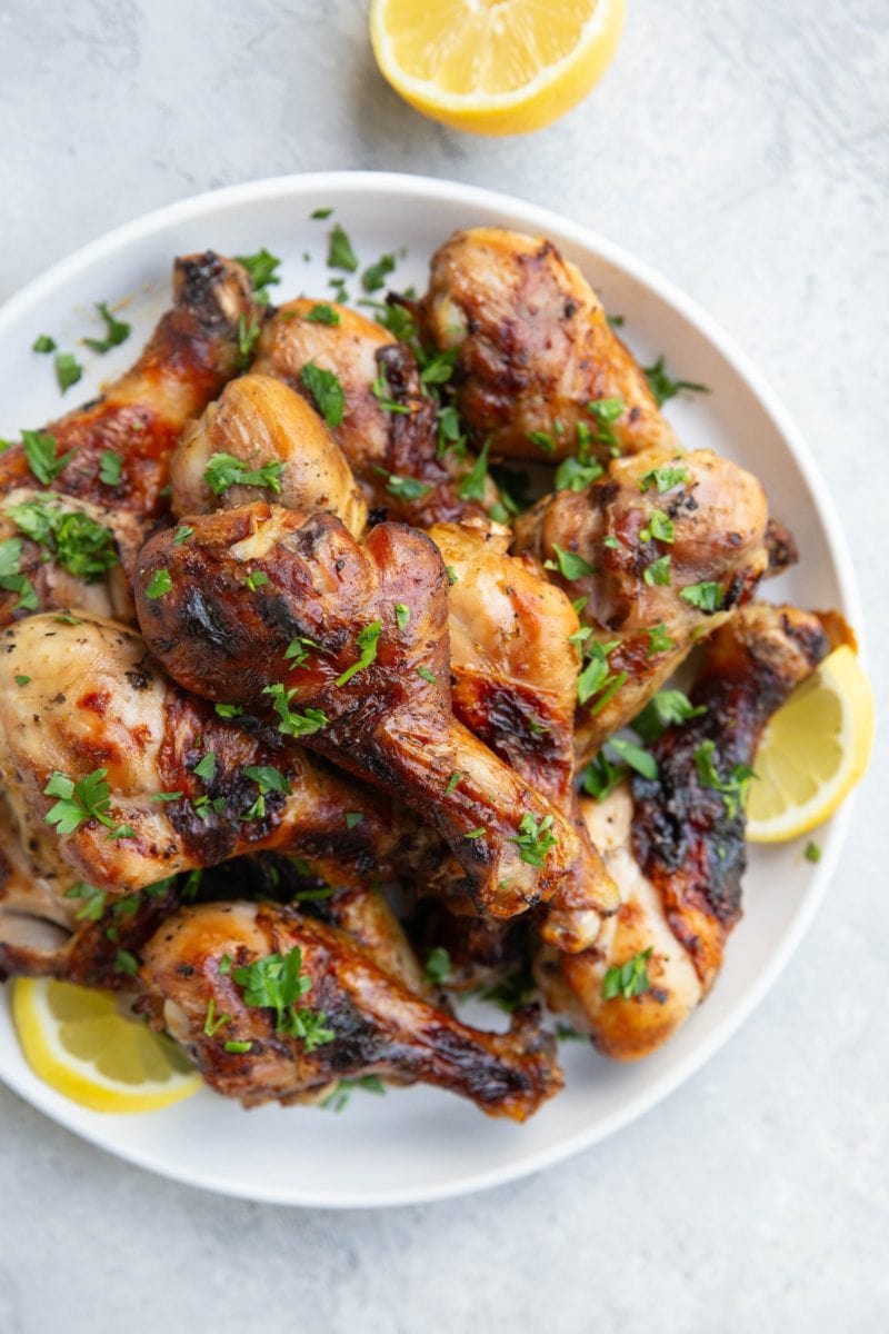 Plate of chicken drumsticks with fresh parsley sprinkled on top and slices of lemons to the side. Ready to serve with side dishes.