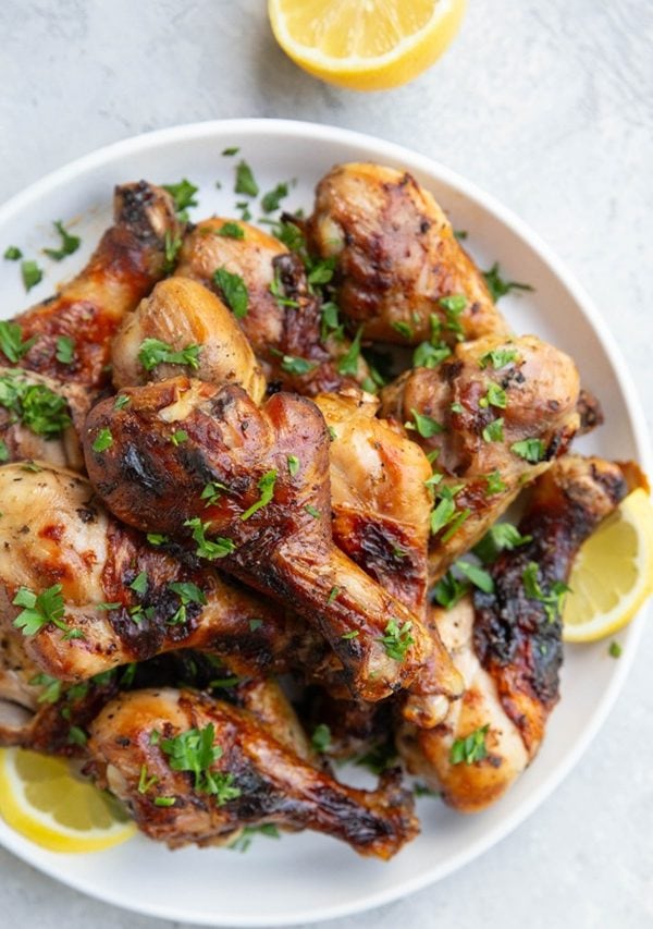 Plate of grilled chicken drumsticks sprinkled with chopped parsley.