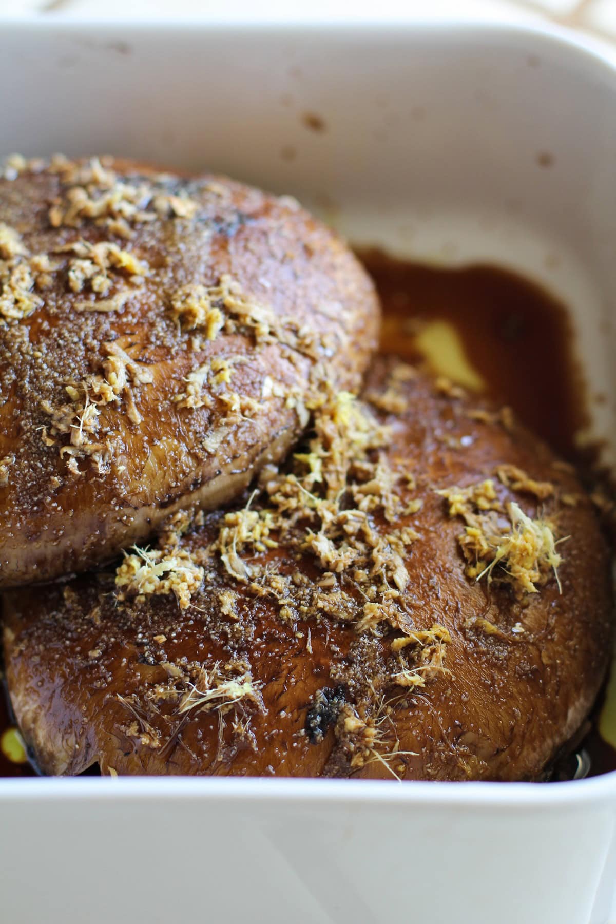 Portobello mushrooms in a large casserole dish with marinade on top.