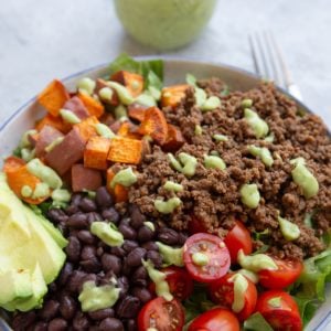 Big bowl of salad greens, brown rice, black beans, seasoned ground beef, tomatoes, and everything is drizzled with lime herb avocado dressing.