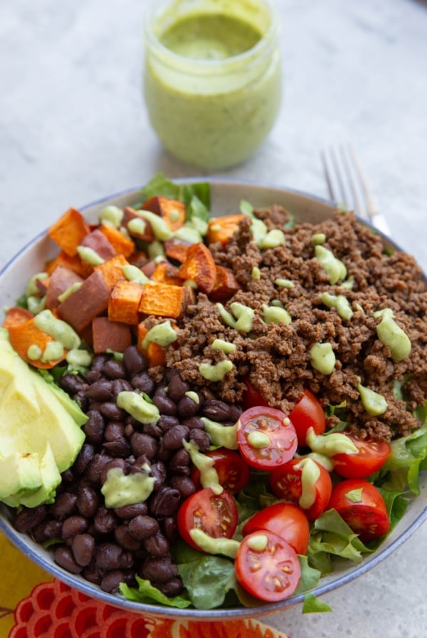 Big bowl of salad greens, brown rice, black beans, seasoned ground beef, tomatoes, and everything is drizzled with lime herb avocado dressing.