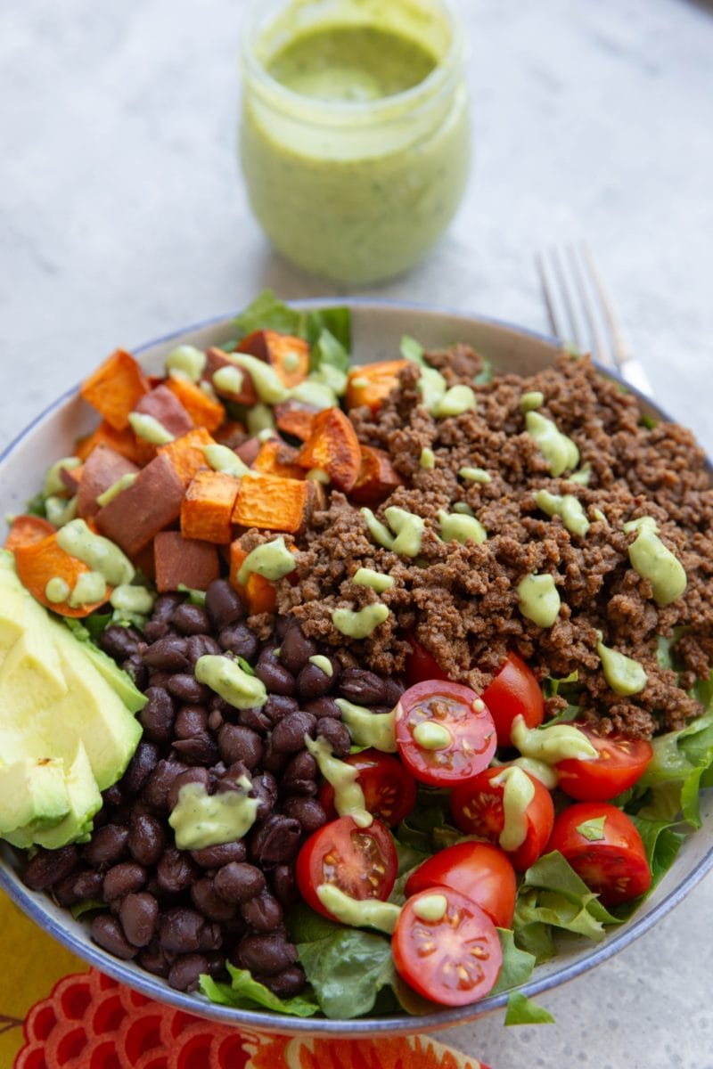 Big bowl of salad greens, brown rice, black beans, seasoned ground beef, tomatoes, and everything is drizzled with lime herb avocado dressing.