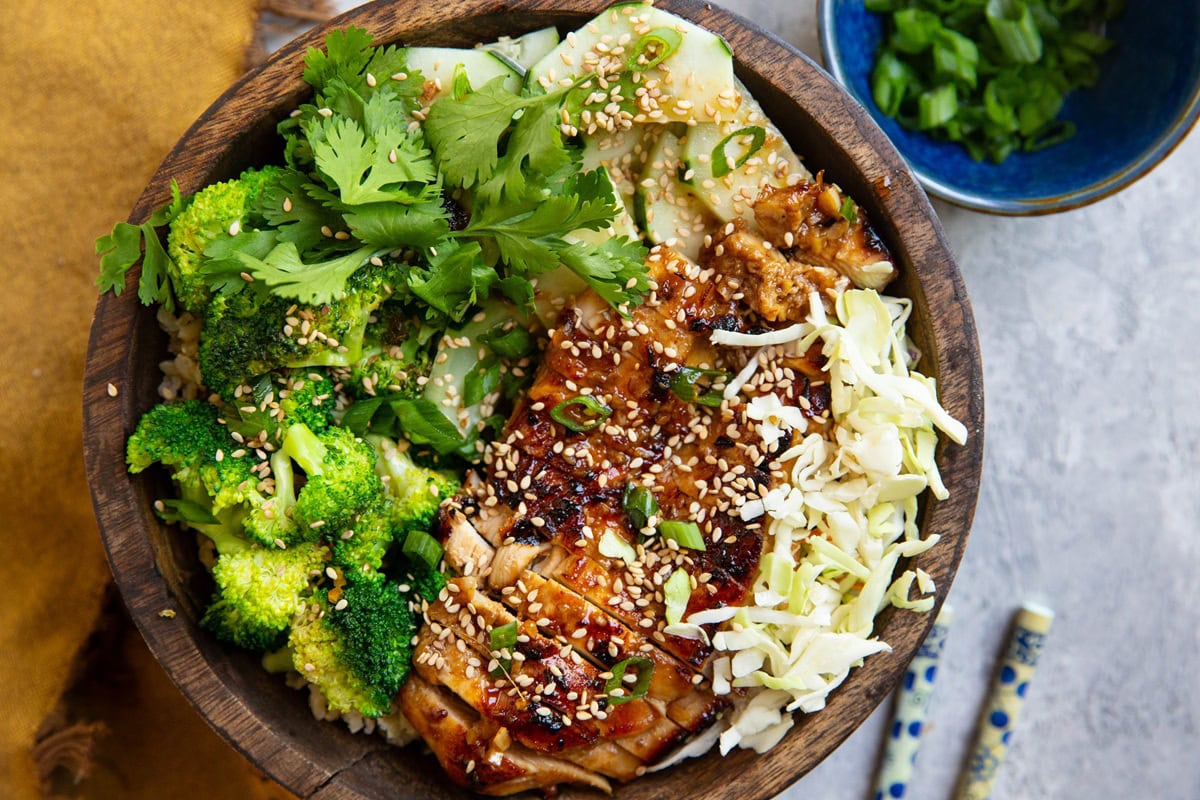 Korean BBQ Chicken in a bowl sprinkled with sesame seeds and green onions, alongside fresh vegetables.