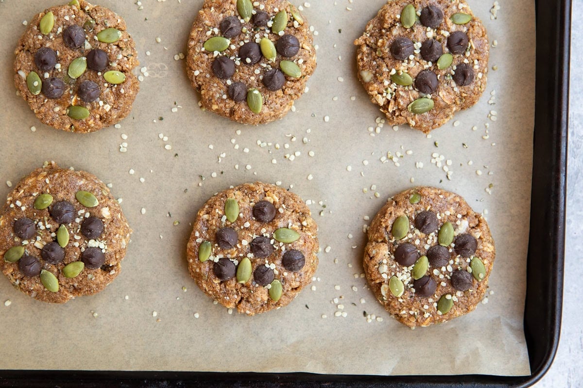 No bake breakfast cookies topped with chocolate chips and pumpkin seeds on a parchment lined baking pan.