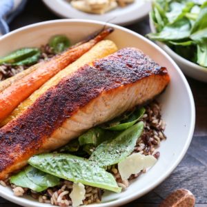 Big bowl of salmon Caesar salad with roasted carrots and wild rice. More salad in the background.