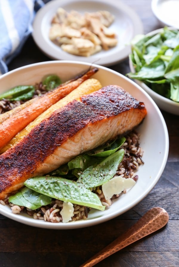 Big bowl of salmon Caesar salad with roasted carrots and wild rice. More salad in the background.