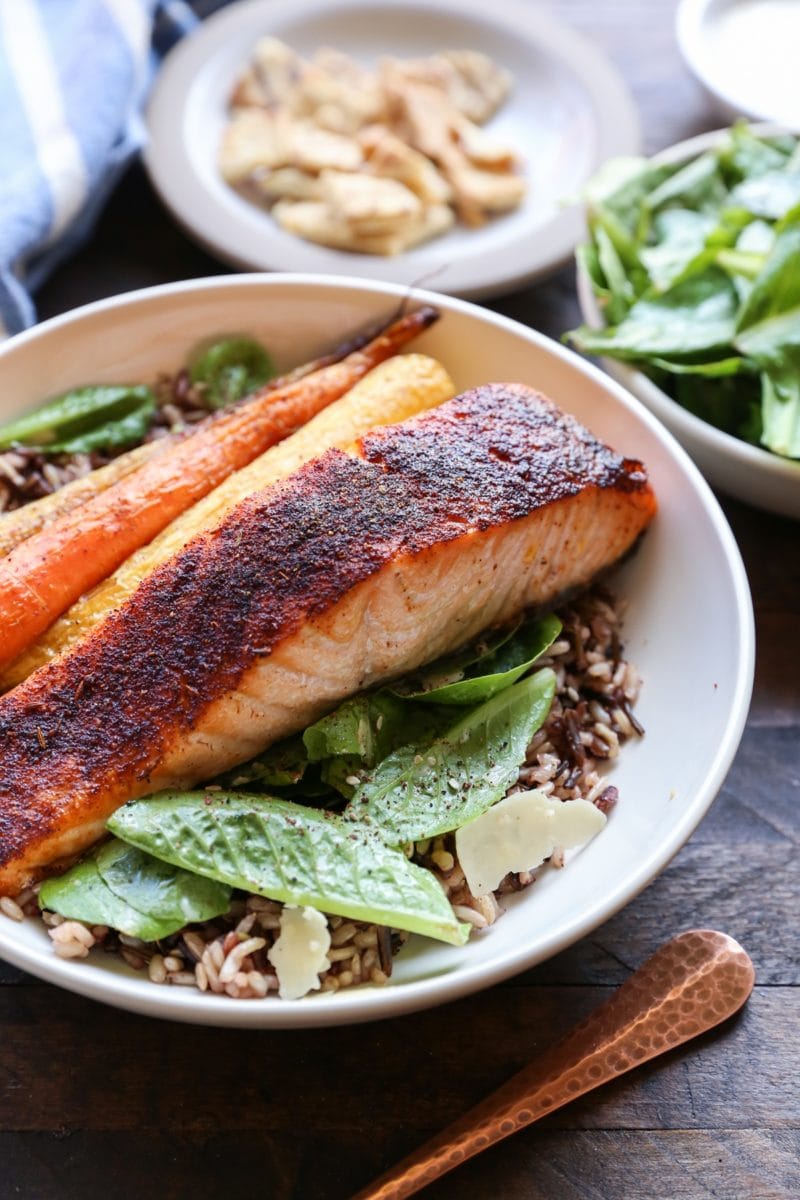 Big bowl of salmon Caesar salad with roasted carrots and wild rice. More salad in the background.