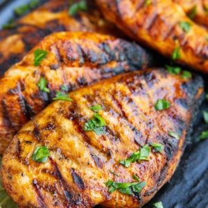 Four grilled chicken breasts sitting on a black plate sprinkled with chopped parsley. Ready to serve.