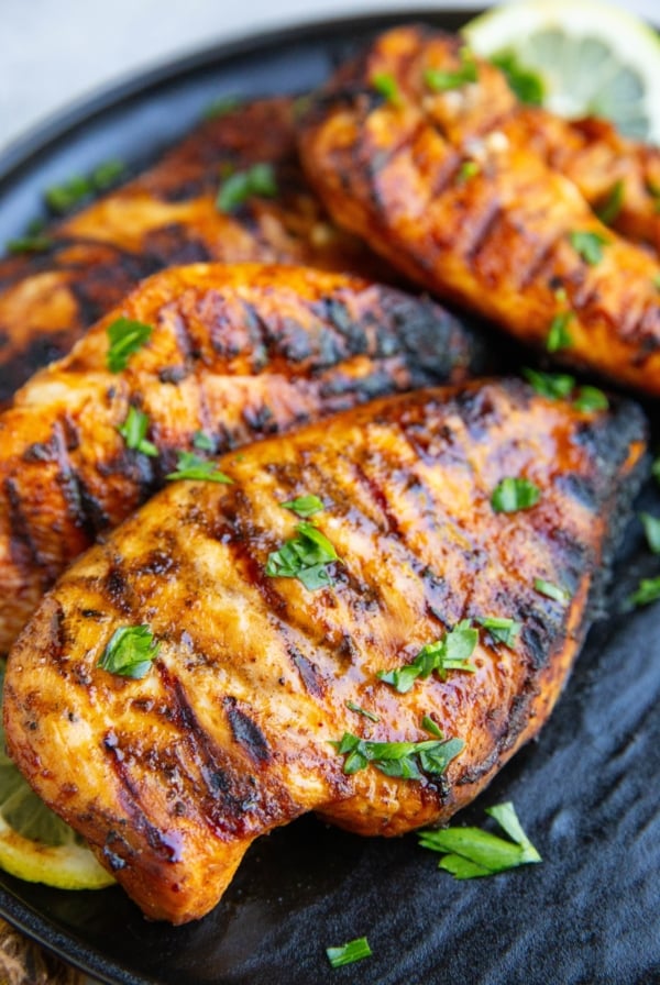 Four grilled chicken breasts sitting on a black plate sprinkled with chopped parsley. Ready to serve.