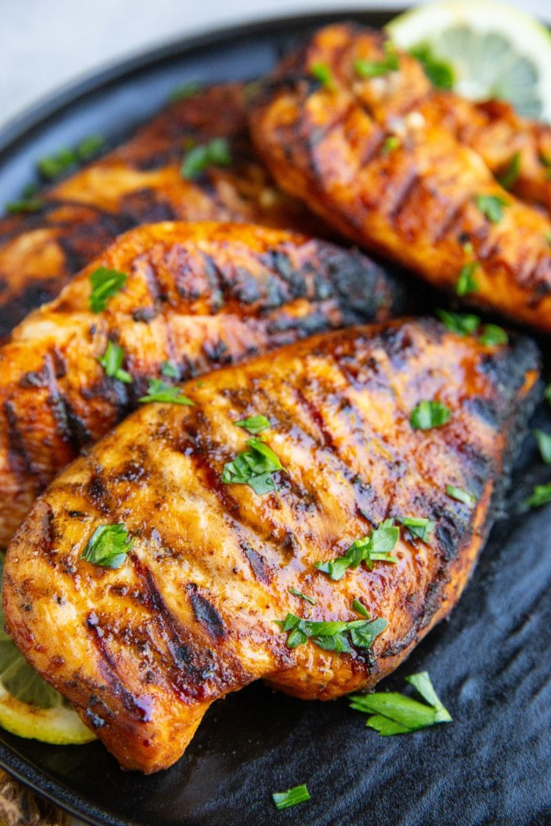Four grilled chicken breasts sitting on a black plate sprinkled with chopped parsley. Ready to serve.