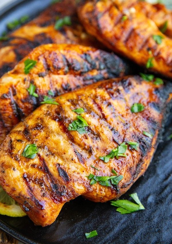 Grilled chicken on a plate with chopped fresh herbs sprinkled on top, ready to serve.