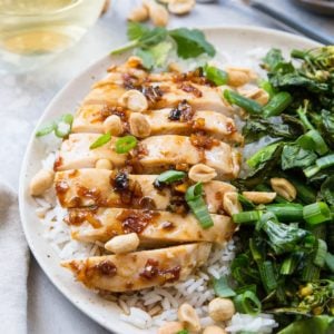 Lemongrass chicken sliced on a plate with white rice and broccolini. A glass of white wine in the background.