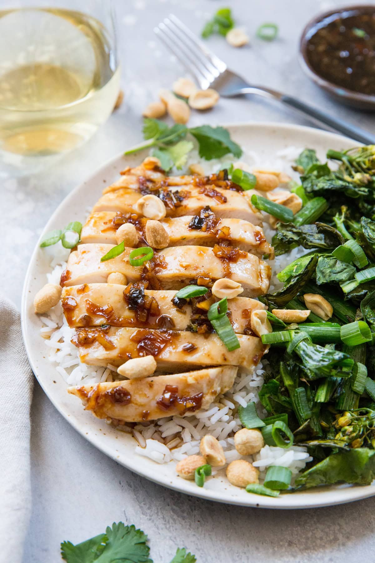 Lemongrass chicken sliced on a plate with white rice and broccolini. A glass of white wine in the background.