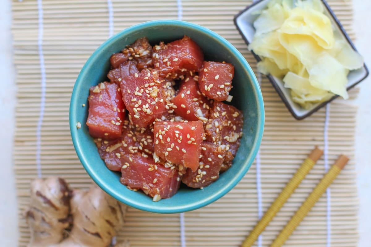 Bowl of ahi poke sprinkled with sesame seeds. Fresh ginger and chop sticks to the side.
