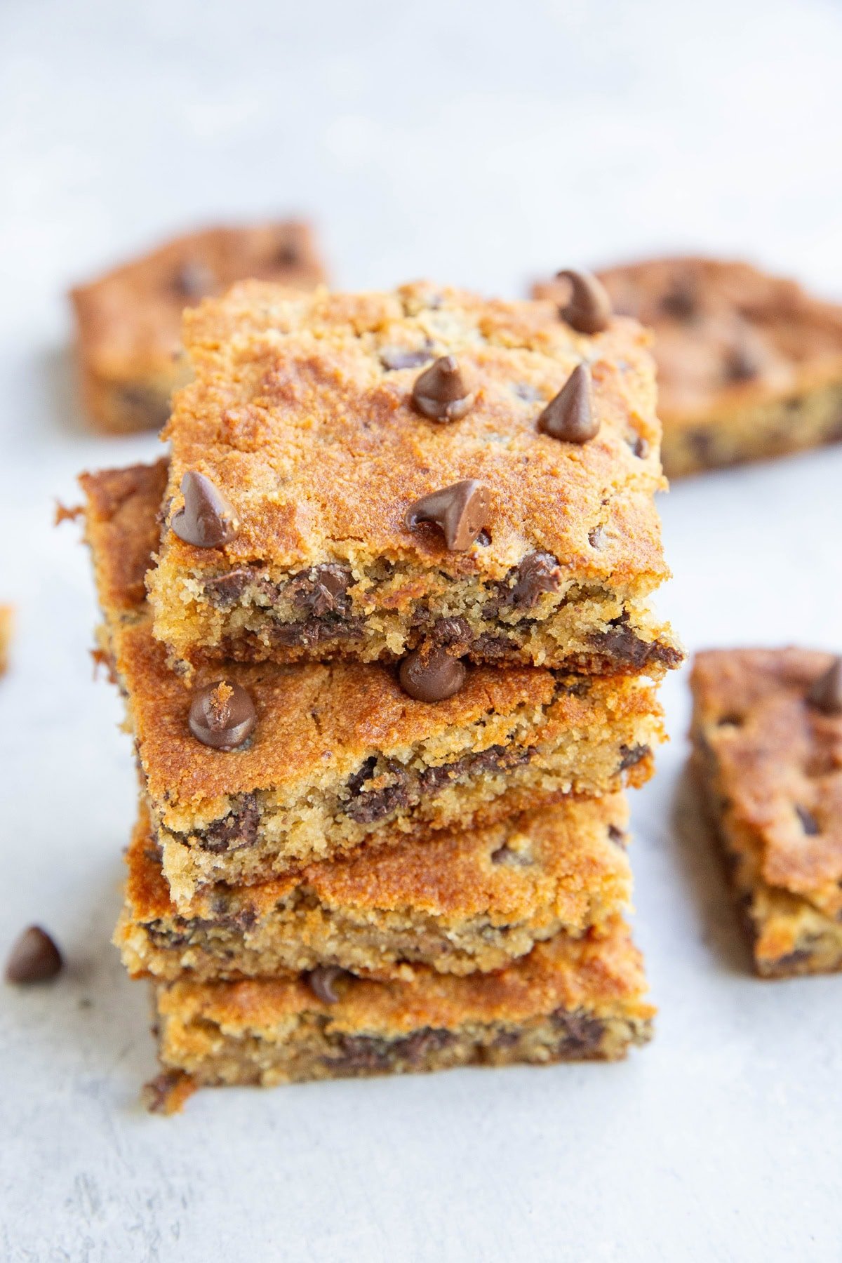 Stack of four grain free chocolate chip blondies with other blondies to the side.