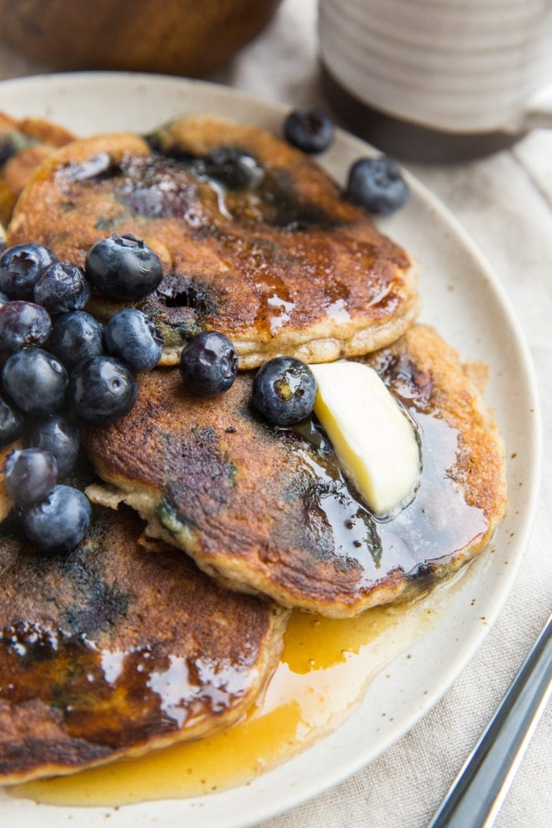 Almond flour pancakes on a plate with fresh blueberries, melted butter, and honey. A fork to the side, ready to serve.
