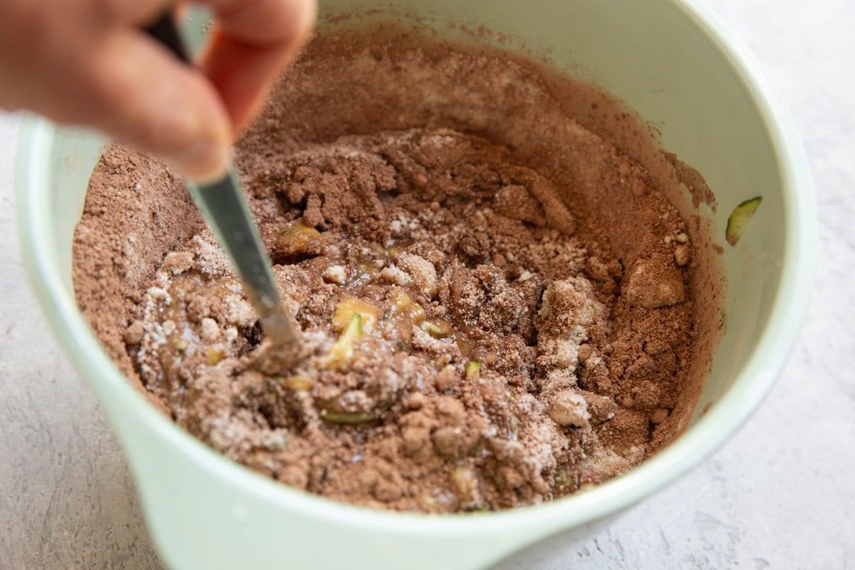 Hand stirring chocolate zucchini bread batter in a large mixing bowl.
