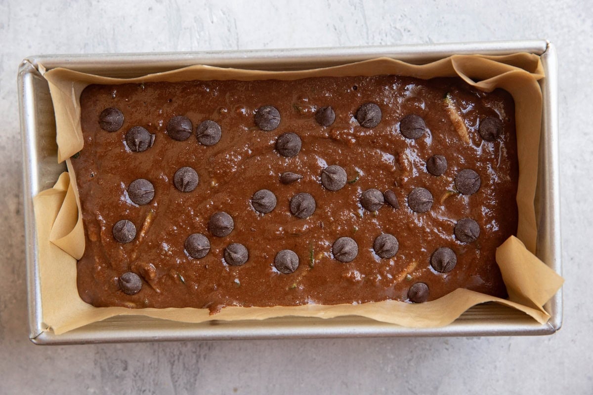 Loaf pan lined in parchment paper with chocolate zucchini bread batter inside.