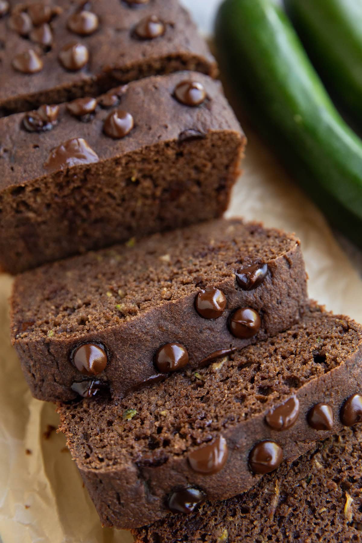 Loaf of chocolate zucchini bread cut into slices with fresh zucchini in the background.