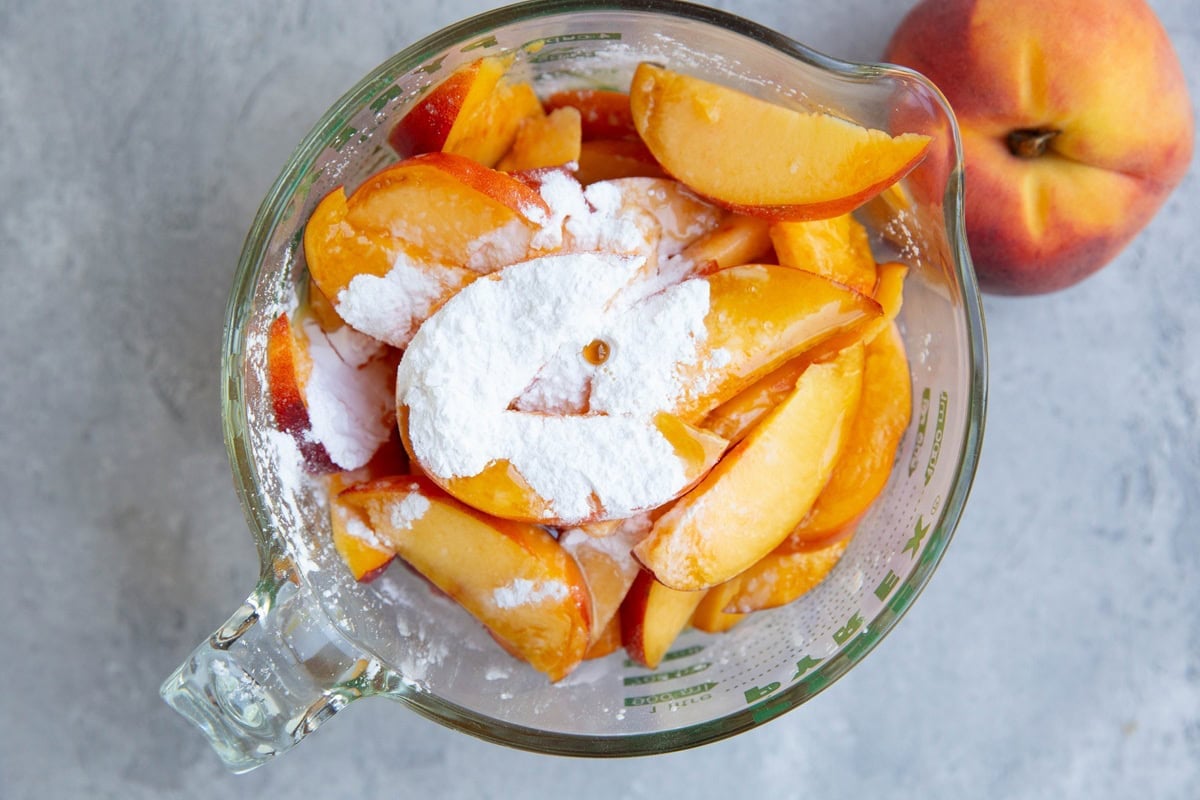 Large measuring cup full of peach slices, flour, and pure maple syrup to make peach pie filling for a fruit crisp.