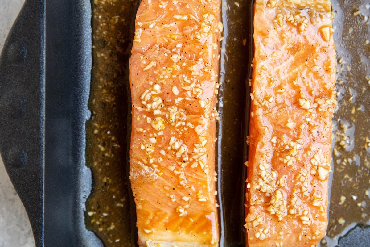 Two marinated salmon filets in a large baking dish, ready to go into the oven.