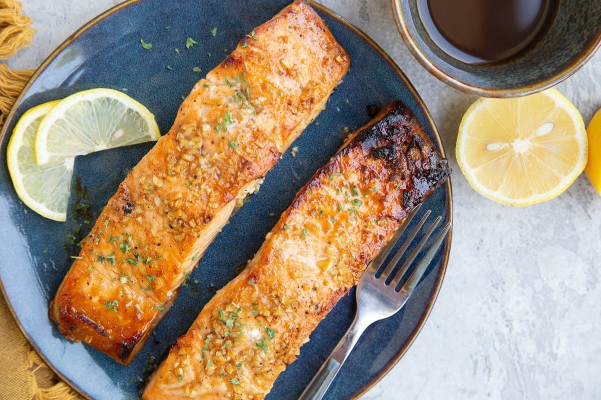 Blue plate with two balsamic glazed salmon filets on top. Slices of fresh lemon on the plate and a lemon cut in half to the side.