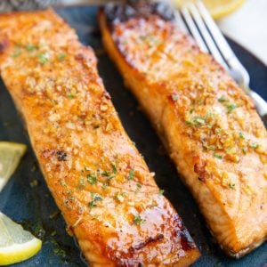 Balsamic glazed salmon on a plate with a fresh lemon in the background and a small bowl of glaze.