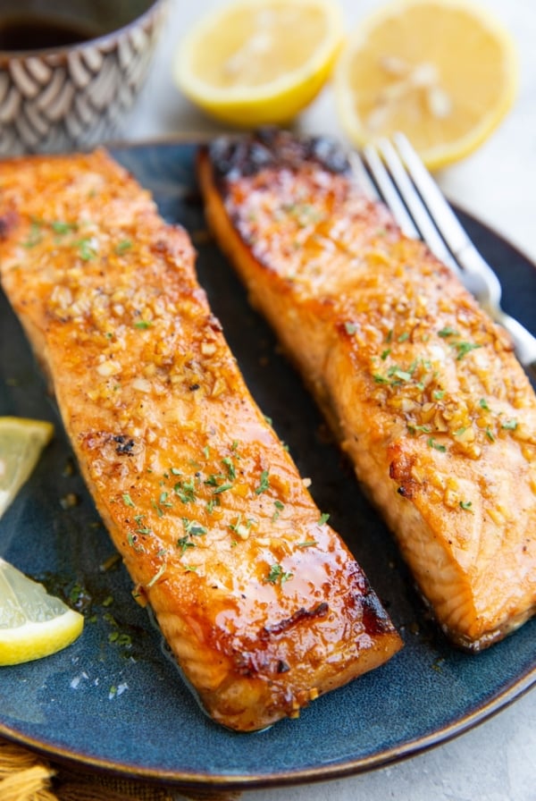Balsamic glazed salmon on a plate with a fresh lemon in the background and a small bowl of glaze.