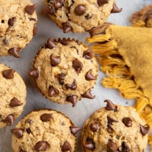 Chocolate Chip Banana Oat Muffins on a surface with a golden napkin to the side. Ready to eat.