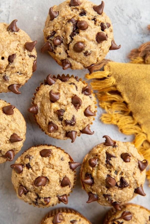 Chocolate Chip Banana Oat Muffins on a surface with a golden napkin to the side. Ready to eat.